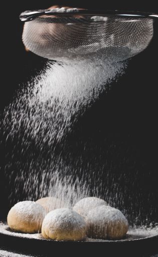 A vertical shot of a hand pouring powder over cookies