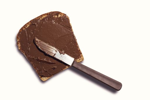A top view of a bread slice with chocolate spread and a knife on it isolated on white background
