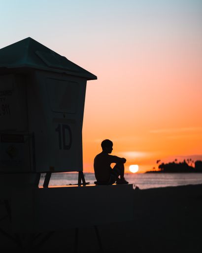 A silhouette of a boy sitting near the cabin on the sunset background