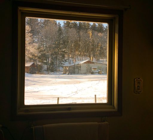 A window overlooking a hut in a forest covered with snow at golden hour