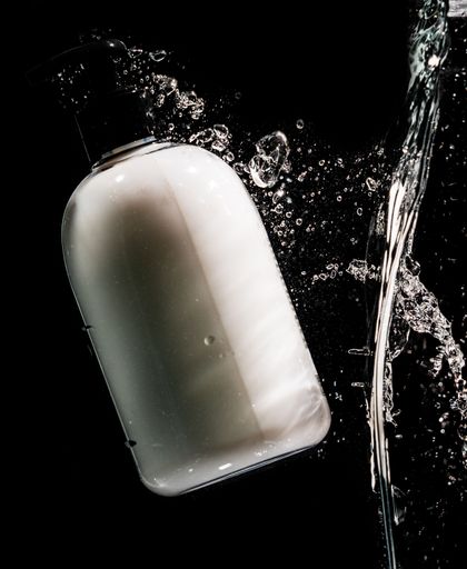 A white hand cream bottle splashing with water droplets on the black background