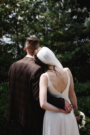A vertical shot of a bride with her head on the groom's shoulder while holding hands