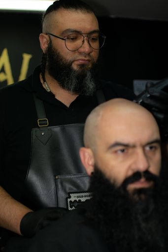 A barber giving a professional shave to an adult male with a full beard
