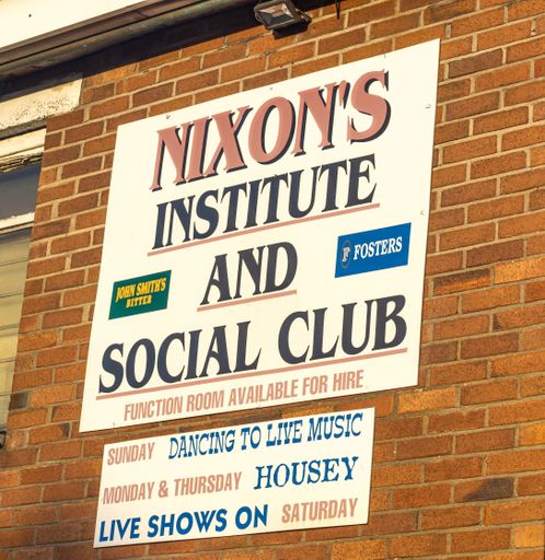 A sign hanging on a brick wall with the text 'Nixon's Institute and Social Club'