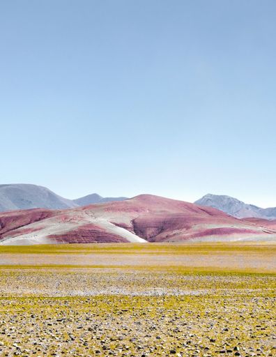 A landscape of a deserted mountain range with purple and yellow hues under the sunlight