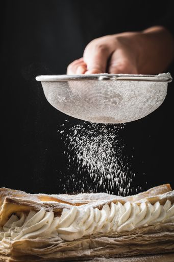 A closeup shot of a persons hand putting powder on a creamy dessert