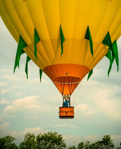 A vibrant yellow hot air balloon with unique orange and green patterns soaring in the sky