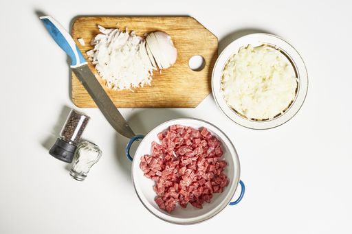 A top view of chopped onion, ground meat, and seasonings for manti dumplings on a white surface