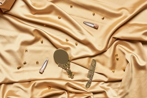 A top view of a decorative metal mirror and a hair comb on a brown silk fabric