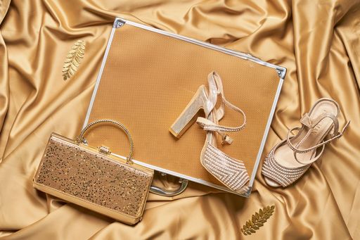 A top view of a brown metal briefcase with elegant high heels and a purse on the silk brown fabric