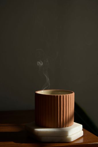 A close-up shot of a ceramic pot emitting a thin stream of white smoke from a lit candle inside