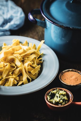 A top view shot of fettuccine with sauces and a blue pan next to it