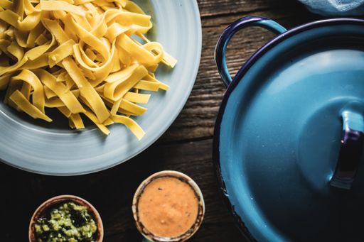 A top view shot of fettuccine with sauces and a blue pan next to it