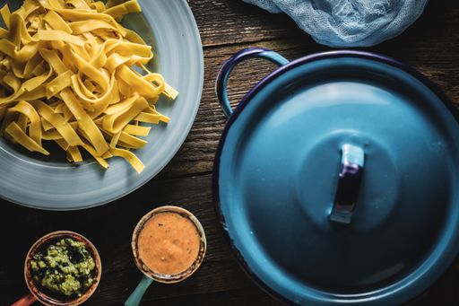 A top view shot of fettuccine with sauces and a blue pan next to it