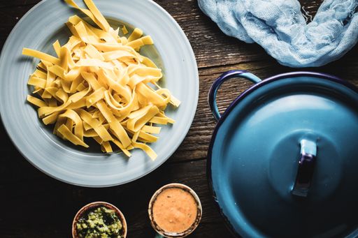 A top view shot of fettuccine with sauces and a blue pan next to it