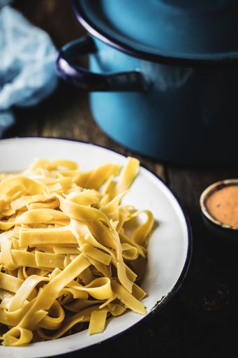 A vertical shot of fettuccine on the plate next to the sauce and a blue pan