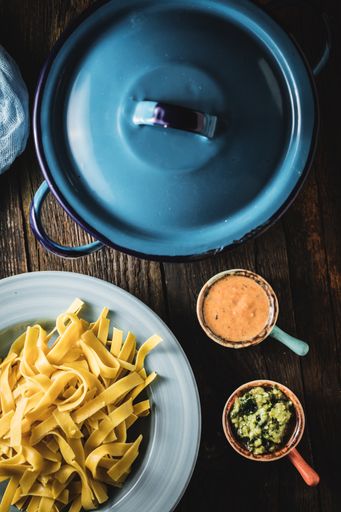 A vertical shot of fettuccine on the plate next to the sauce and a blue pan