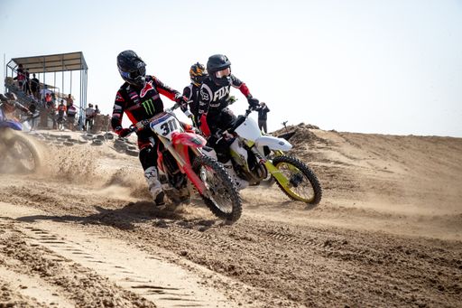 Motorcross riders on sand racing with motorbikes and protective gear
