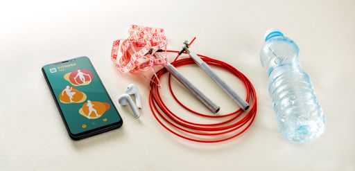 A top view of a smartphone showing a fitness app next to jump rope and bottle of water on the desk