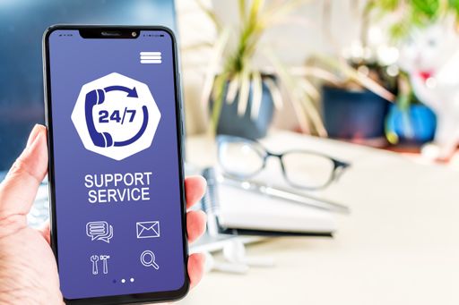 A selective focus of a hand holding a smartphone showing a support service app at a desk