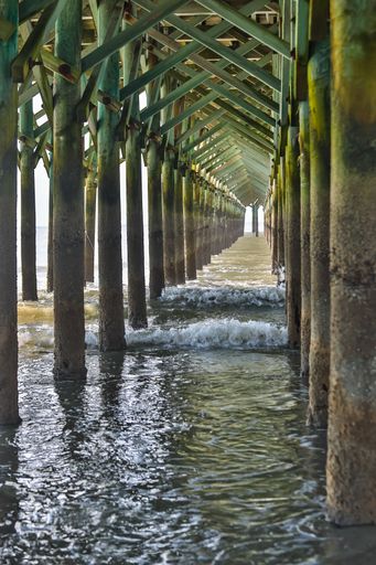 The sun shining through a pier at Myrtle Beach, SC as the surf rolls in
