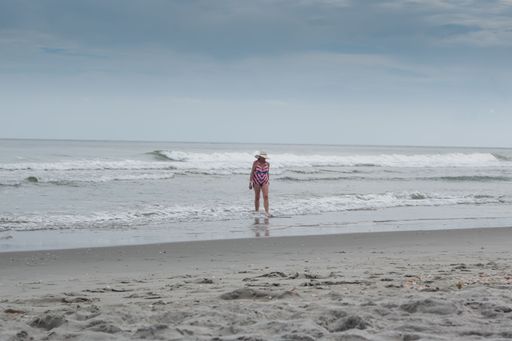 A woman in a beach hat walking in the surf at Myrtle Beach, SC