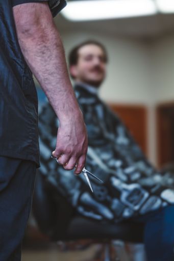 A grayscale of a barber approaching his client with a pair of scissors in his hand