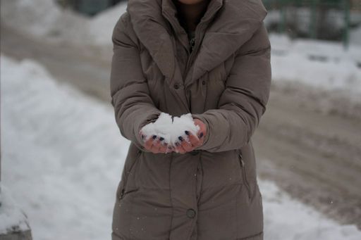 A shallow focus shot of a Caucasian girl wearing winter clothes holding white snow, standing outdoors
