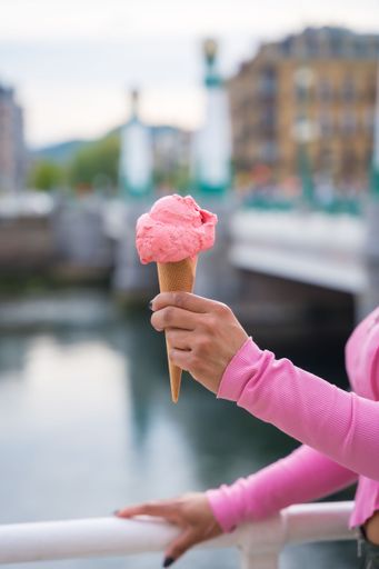 A closeup of a person holding a pink ice cream cone against a river