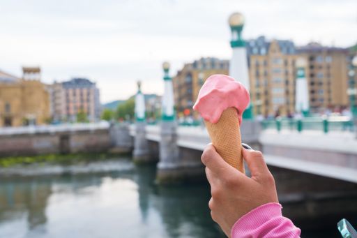 A closeup of a person holding a pink ice cream cone against a river