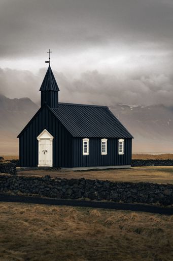 A beautiful, scenic view of a black church perched atop a lush grassy field: Iceland