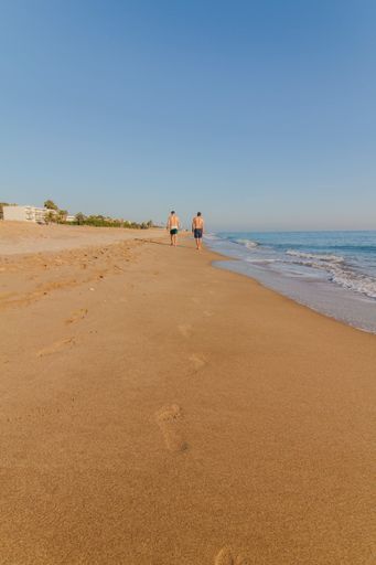 A rearview of two male tourist walking with footprints on the sandy beach