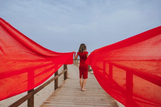 A rear view of a barefooted woman holding red long clothes while standing on a wooden footbridge