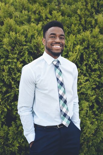 A vertical shot of a handsome African-American male posing on a green thuja background