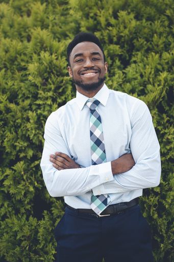 A vertical shot of a handsome African-American male posing on a green thuja background