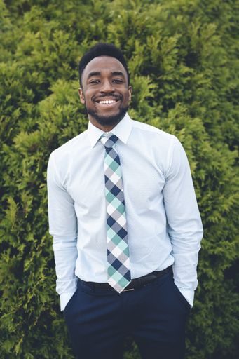 A vertical shot of a handsome African-American male posing on a green thuja background