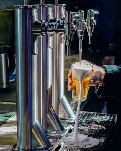 A vertical closeup of a man pouring a cold beer from a tap at a bar