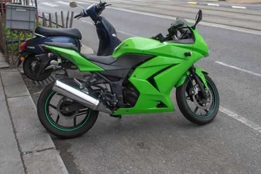 A vibrant green motorcycle with a dark blue motor scooter parked on the side of a street. Vienna.