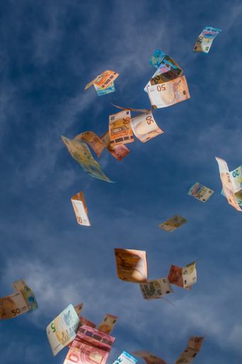 A vertical shot of falling money from blue sky with clouds
