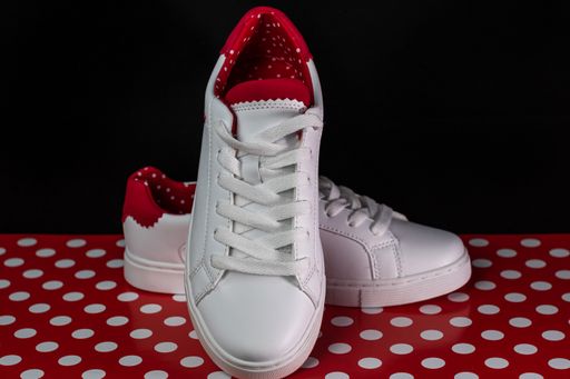 A closeup of a pair of white sports shoes isolated on the red background with white dots in Bucharest, Romania