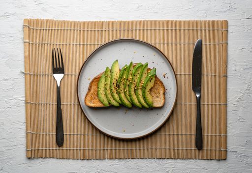A top view of a delicious avocado toast on a white plate, with fork and knife