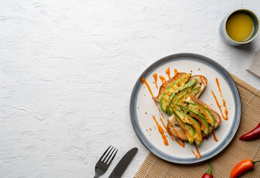 A top view of a delicious avocado toast covered in spicy sauce on a white plate, copy space