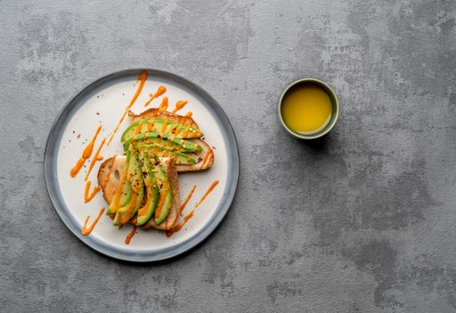 A top view of a delicious avocado toast covered in spicy sauce on a white plate, on a  grey surface