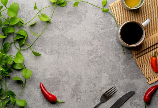A top view of  a grey surface with a cup of coffee, red peppers, and a plant, copy space