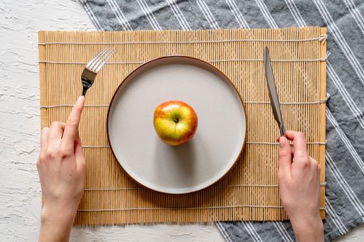 A top view of a fresh apple on a white plate, with someone using the fork and knife