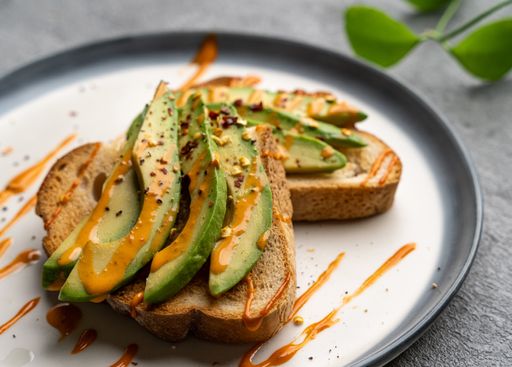 A closeup of a delicious avocado toast covered in spicy sauce on a white plate