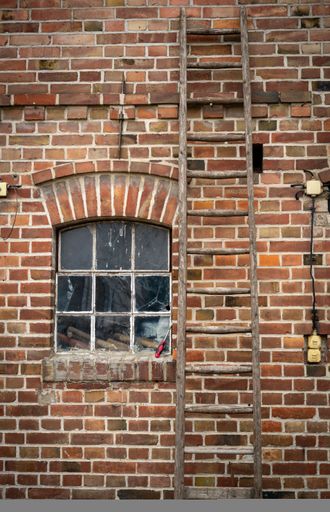 A ladder leaning on a red brick building with a window