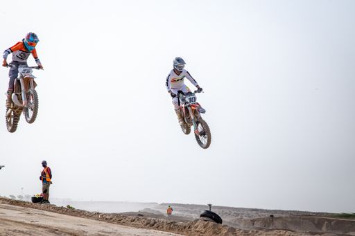 motorcross riding motorbike on sandy track during the day jumping