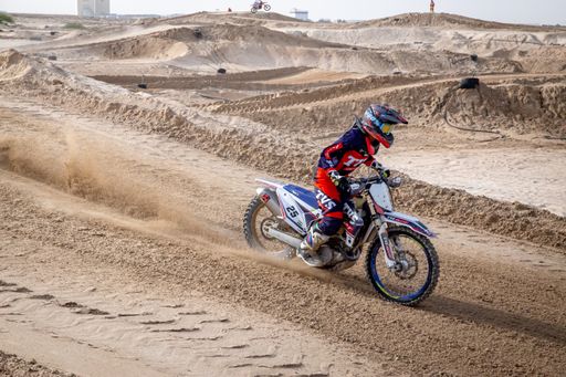 motorcross riding motorbike on sandy track during the day jumping