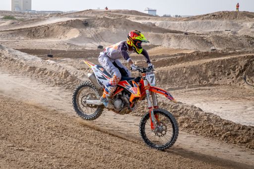 motorcross riding motorbike on sandy track during the day jumping